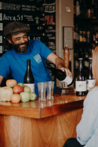 Smiling bar man and owner serving up cider at Little Green Men in Deloraine