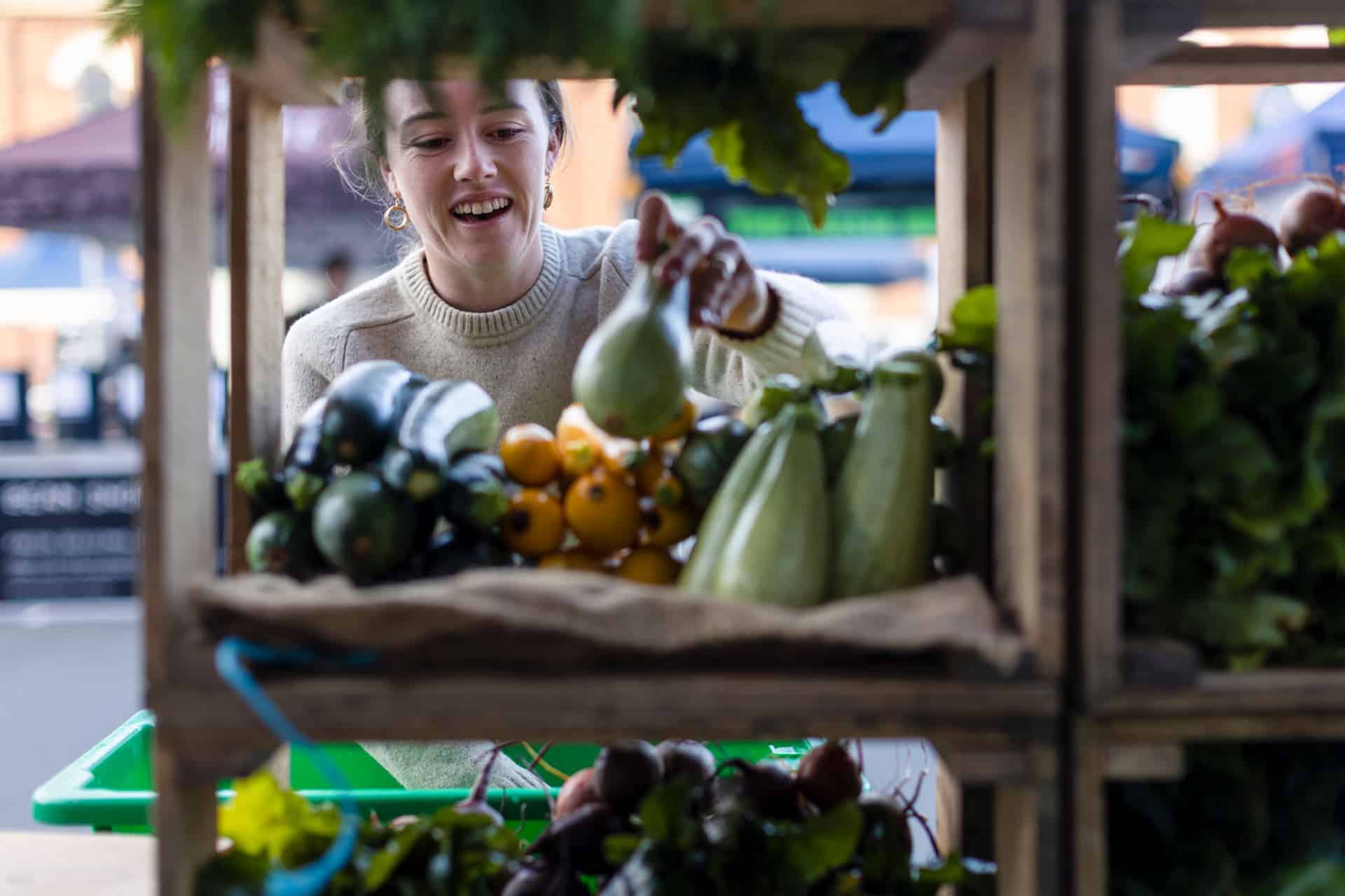 Woman selecting fresh vegetables from a market stall display at Harvest Market Launceston.